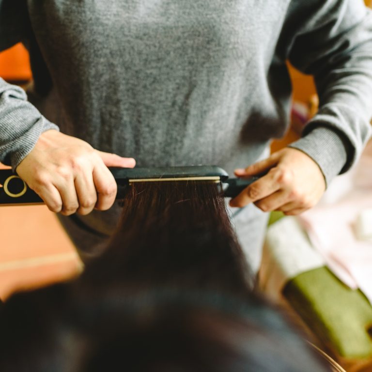 Hairdresser smoothing a woman's hair with a hair straightener.